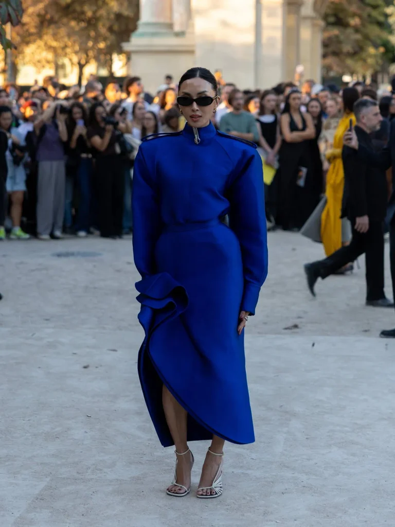 Woman in a cobalt blue midi dress with big shoulders, sunglasses, and white strappy heels